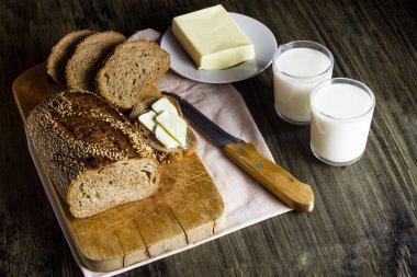 Bütün tahıl ekmeği ile susam ahşap bir gemide. Tereyağı. Cam bardak süt.