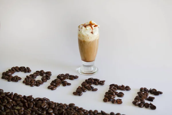 Iced coffee or Frappuccino with whipped cream and syrup .Coffee word , text made of roasted coffee beans isolated on white background.