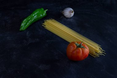 Makarna arka planında spagetti, yeşil biber, domates ve sarımsak var. Arka planda fotokopi alanı var. Sağlıklı yiyecek kavramı..