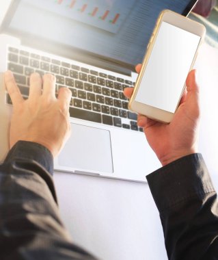 Finans raporunu analiz etmek için bilgisayar ve akıllı telefon kullanan ya da çalışan bir iş adamı, boş ekranlı akıllı telefon