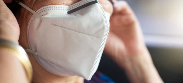 Maske takan üst düzey bir kadın ve hastanede bulanık bir bekleme koltuğu var. İnsanlar doktor, sağlık ve sağlık sigortası konseptiyle tanışmak için bekliyor.