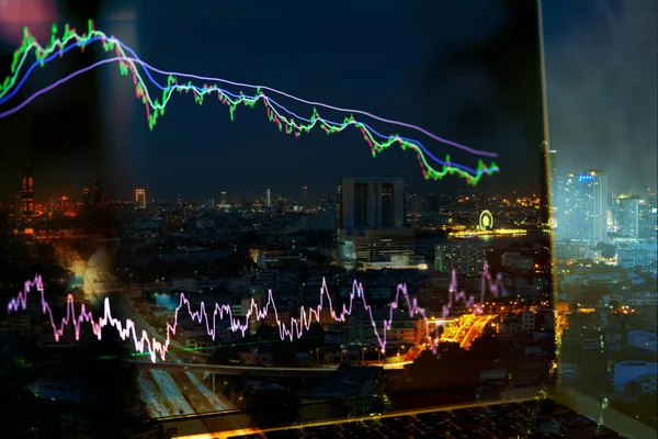 Dizüstü bilgisayar ekranında ema ve rsi göstergelerinin yer aldığı hisse senedi grafiği, ayı piyasasında borsa grafiği ve gerileme eğilimi ve arka planda şehir gece görüntüsü