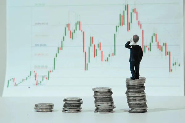 İşadamı ve finansal büyüme konsepti, üst üste madeni paralar ve madeni paraların üzerinde duran minyatür işadamı, beyaz kağıt üzerinde Fibonacci göstergesi olan borsa teknik grafiğini bulanıklaştırdı.