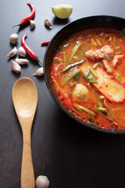 Tayland yemekleri konsepti. Tayland mutfağı tabağı. Tom 'un siyah tabakta lezzetli çorbası, ahşap tabakta pirinç, tahta kepçe ve kaşık, biber, masa arkasında sarımsak, Tayland yemeği dikey resmi.