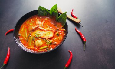 Tayland yemekleri konsepti. Tayland mutfağı tabağı. Tom siyah tabakta lezzetli çorba, ahşap kaşık ve masa arkasında kırmızı biber.