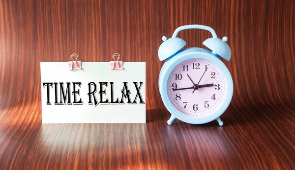 RELAX TIME words on sticker, next to an alarm clock on a wooden table