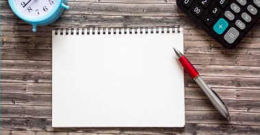 Kalem, alarm saati, hesap makinesi ve tahta arka plandaki not defteri.