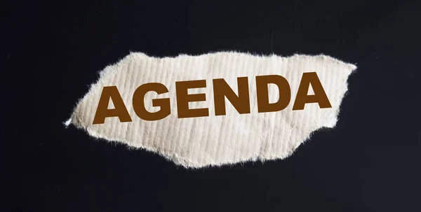 Agenda text printed on brown piece of paper and black background