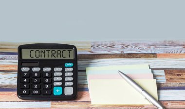 Kontrat, hesap makinesi metni, çıkartma ve kalemle ahşap arka plan. Yazacak bir yer var.