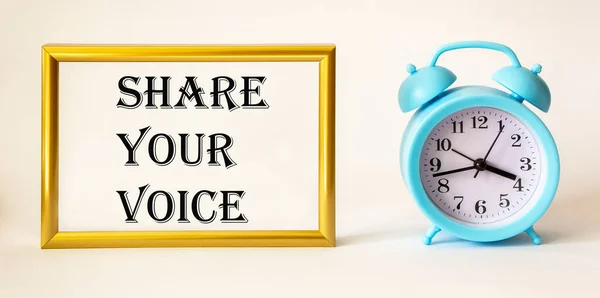 Share your voice written on gold photo frame next to alarm clock on white background.