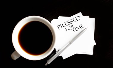 Ofis masasında kahve fincanı ve malzeme var. Zaman için sıkıştırılmış metin için yukarıdan görünüm