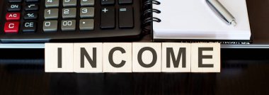 INCome - tahta blokta dizüstü bilgisayar, hesap makinesi ve not defteri ile iş konsepti metni