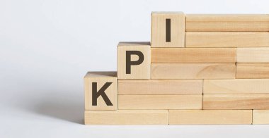 Beyaz masanın üzerinde KPI harfleri olan üç tahta küp..