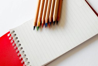 Beyaz arkaplandaki deftere renkli kalemler