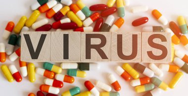 Tahta bloklar ve beyaz arka planda VIRUS harfleri ve hap yığını