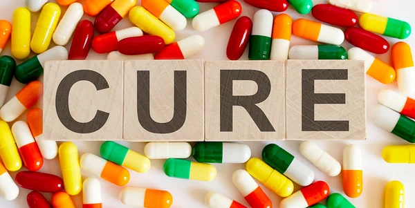 Wooden blocks with CURE lettering and pile of pills on white background