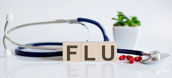 Flu単語は木製の立方体と聴診器と杭に書かれています 医学的概念 — ストック写真