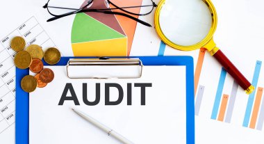 AUDIT raporları, boş kağıt, veri tabloları ve grafikler, büyüteç, madeni paralar - ofis çalışma alanı görünümünün tam üstünde