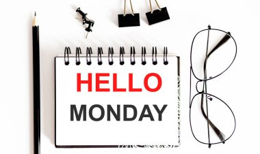 Bir fincan kahve, kalem, güneş gözlüğü ve defterin üst görüntüsü beyaz ahşap arka planda HELLO ile Pazartesi günü yazılmış.