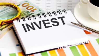INVEST metni. Üst görünüm ofis masası, pazarlama planı için iş grafiği programı. Kitap, kalem, sade kahve, ataç, büyüteç ve dolar.