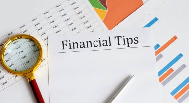 FINANCIAL TIPS İş Raporları, boş kağıt, veri tabloları ve çizelgeler, büyüteç, ofis çalışma alanının tam üstünde