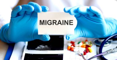 İçinde MIGRAINE malzemeleri, haplar ve stetoskop olan bir kart. Tıbbi konsept.