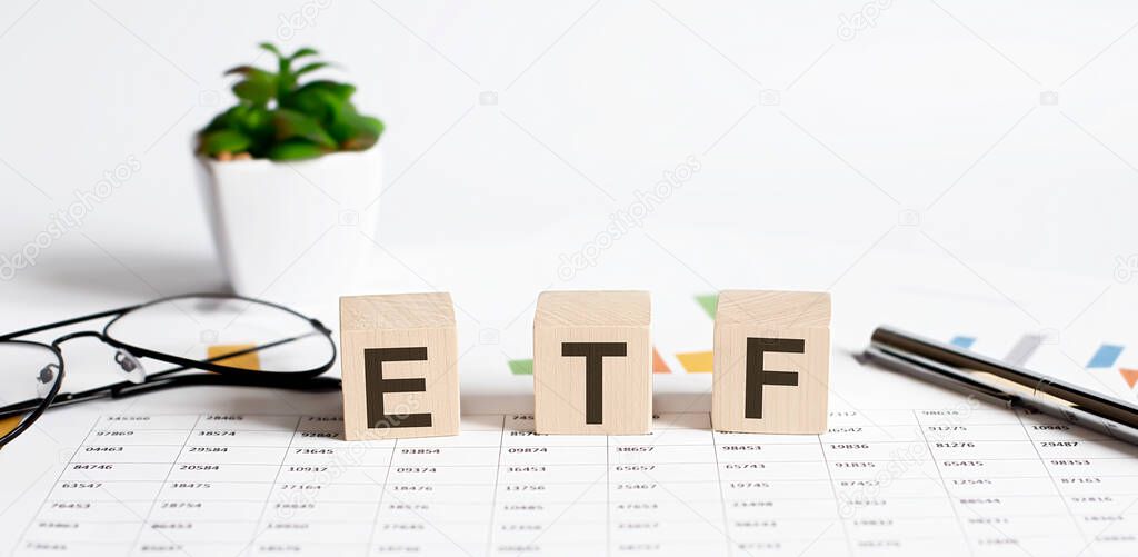 ETF word concept written on wooden blocks, cubes on a light table with flower ,pen and glasses on chart background