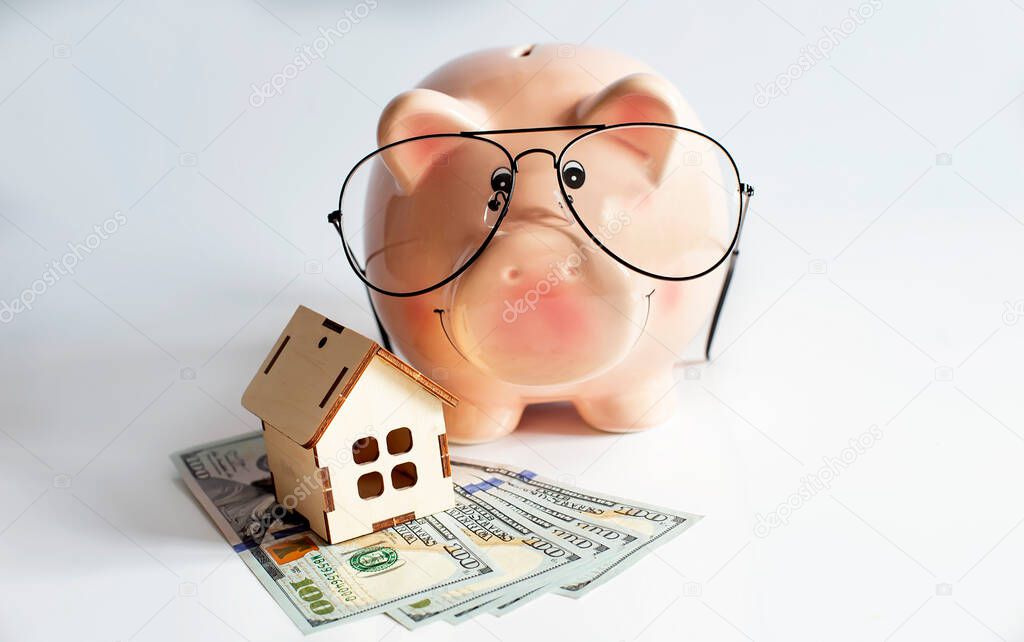 Piggybank with wooden house and dollars. Isolated on white background