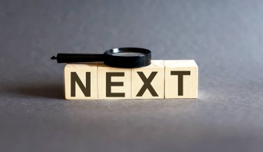 Kelime bloğu NEXT ve gri arka planda büyüteç. Gelir, giderler, vergi, mali veriler.