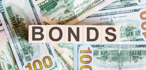 Concept words BONDS on wooden blocks on a beautiful background from dollar bills. Business