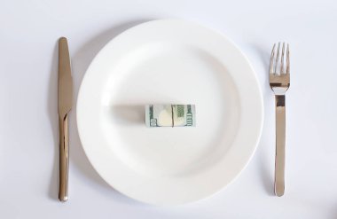 Beyaz arka planda çatal ve bıçak arasındaki beyaz tabakta bir dolarlık banknot, iş konsepti.