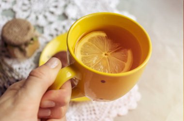 Siyah bardağı sıcak limon çayıyla tutan kadınların elleri..