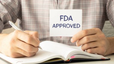 Elinde FDA 'nın yeşil arka planda onayladığı bir kağıt var.