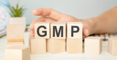 İyi İmalat Uygulaması. Tahta küplerle ilgili kelime GMP, yansıtıcı bir yüzeyde duran küpler, arka planda bir iş diyagramı. İş ve finans kavramı
