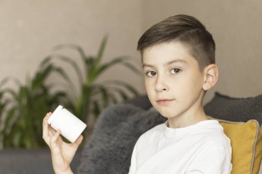 Hasta Çocuk kanepede oturur ve elinde haplarla kavanoza bakar. Soğuk algınlığı ve grip.