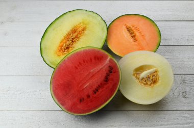Lezzetli organik kavunlar ve karpuz beyaz ahşap arka planda ikiye bölünmüş.