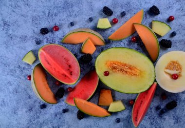 Taze kesilmiş kavunlar, karpuz ve böğürtlenler mavi taştan bir arka planda. 