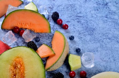 Taze kesilmiş kavun, karpuz, böğürtlen ve buz küpleri mavi taştan arka planda. Boşluk ve metin alanını kopyala