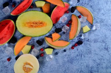 Taze kesilmiş kavun, karpuz, böğürtlen ve buz küpleri mavi taştan arka planda. Boşluk ve metin alanını kopyala