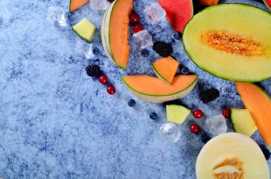 Taze kesilmiş kavun, karpuz, böğürtlen ve buz küpleri mavi taştan arka planda. Boşluk ve metin alanını kopyala
