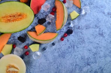 Taze kesilmiş kavun, karpuz, böğürtlen ve buz küpleri mavi taştan arka planda. Boşluk ve metin alanını kopyala