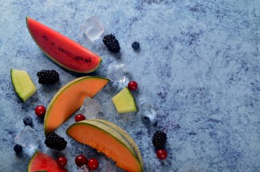 Taze kesilmiş kavun, karpuz, böğürtlen ve buz küpleri mavi taştan arka planda. Boşluk ve metin alanını kopyala