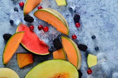 Taze kesilmiş kavun, karpuz, böğürtlen ve buz küpleri mavi taştan arka planda. Boşluk ve metin alanını kopyala