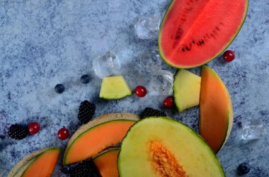 Taze kesilmiş kavun, karpuz, böğürtlen ve buz küpleri mavi taştan arka planda. Boşluk ve metin alanını kopyala