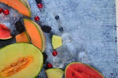 Taze kesilmiş kavun, karpuz, böğürtlen ve buz küpleri mavi taştan arka planda. Boşluk ve metin alanını kopyala