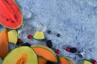 Taze kesilmiş kavun, karpuz, böğürtlen ve buz küpleri mavi taştan arka planda. Boşluk ve metin alanını kopyala