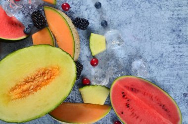 Taze kesilmiş kavun, karpuz, böğürtlen ve buz küpleri mavi taştan arka planda. Boşluk ve metin alanını kopyala