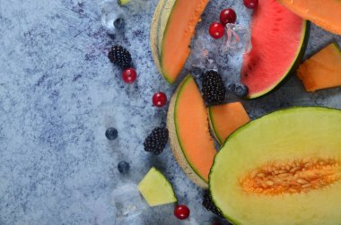 Taze kesilmiş kavun, karpuz, böğürtlen ve buz küpleri mavi taştan arka planda. Boşluk ve metin alanını kopyala