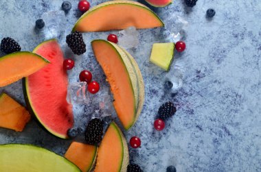 Taze kesilmiş kavun, karpuz, böğürtlen ve buz küpleri mavi taştan arka planda. Boşluk ve metin alanını kopyala
