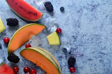 Taze kesilmiş kavun, karpuz, böğürtlen ve buz küpleri mavi taştan arka planda. Boşluk ve metin alanını kopyala